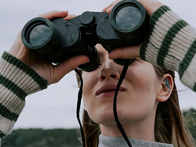 Eine Frau hält mit einem Fernglas nach etwas Ausschau. Foto: (c) Pexels