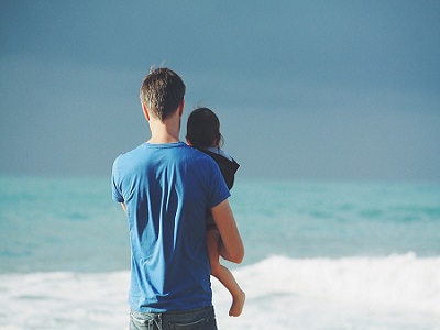 Vater mit Kind auf dem Arm steht am Strand